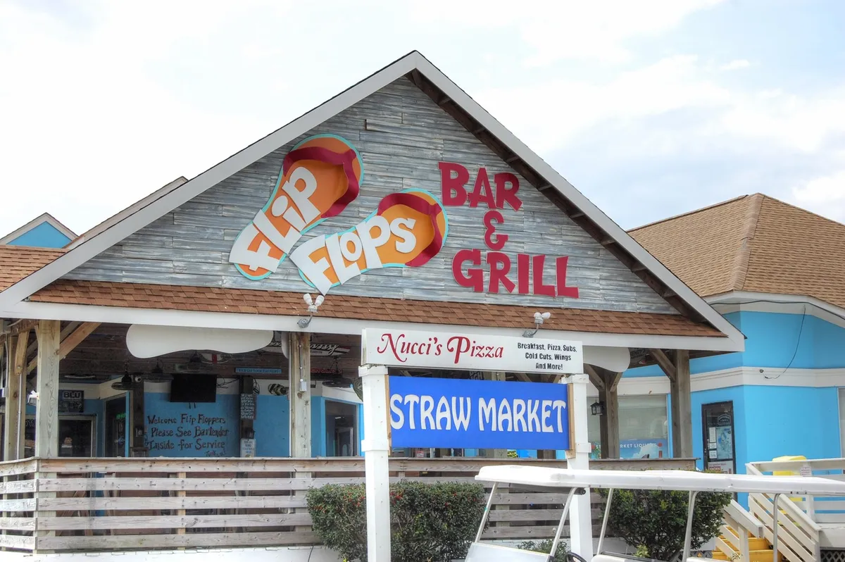 A vibrant outdoor scene showcasing signage for Flip Flops Bar & Grill, Nucci's Pizza, and the Straw Market—local spots ideal for group dining and socializing. The image hints at nearby attractions and culinary adventures.