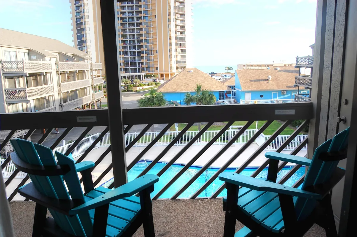 A tranquil poolside scene with Adirondack chairs set near a swimming pool, offering a stunning ocean view in the distance. The arrangement suggests a peaceful spot for relaxation, enjoying the sea breeze, or gathering with family and friends for a sunset barbecue.