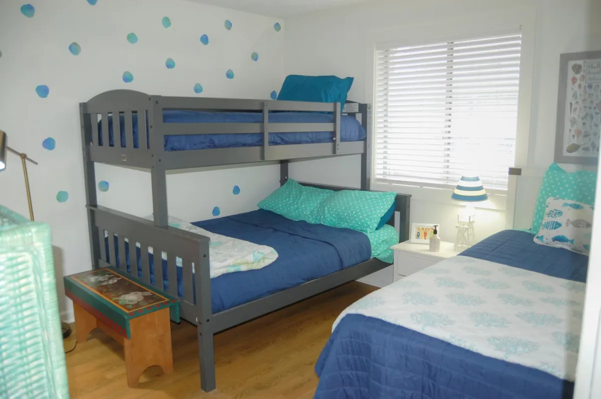 A fun and relaxed second bedroom scene with a twin bed and a bunk bed, colorful wall decor, and a nightstand with a lamp. The space is designed for flexibility and family use, perfect for children or groups. Soft lighting and playful decor contribute to a cozy and inviting vibe, aligning with the section's focus on comfort for every guest.