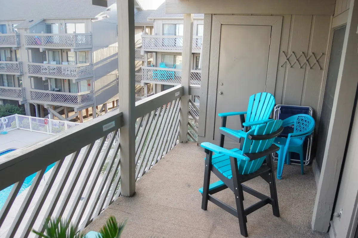 A welcoming exterior balcony scene with turquoise chairs overlooking the pool. The setup encourages guests to gather, chat, or enjoy a meal outdoors while taking in the view of the pool area below.