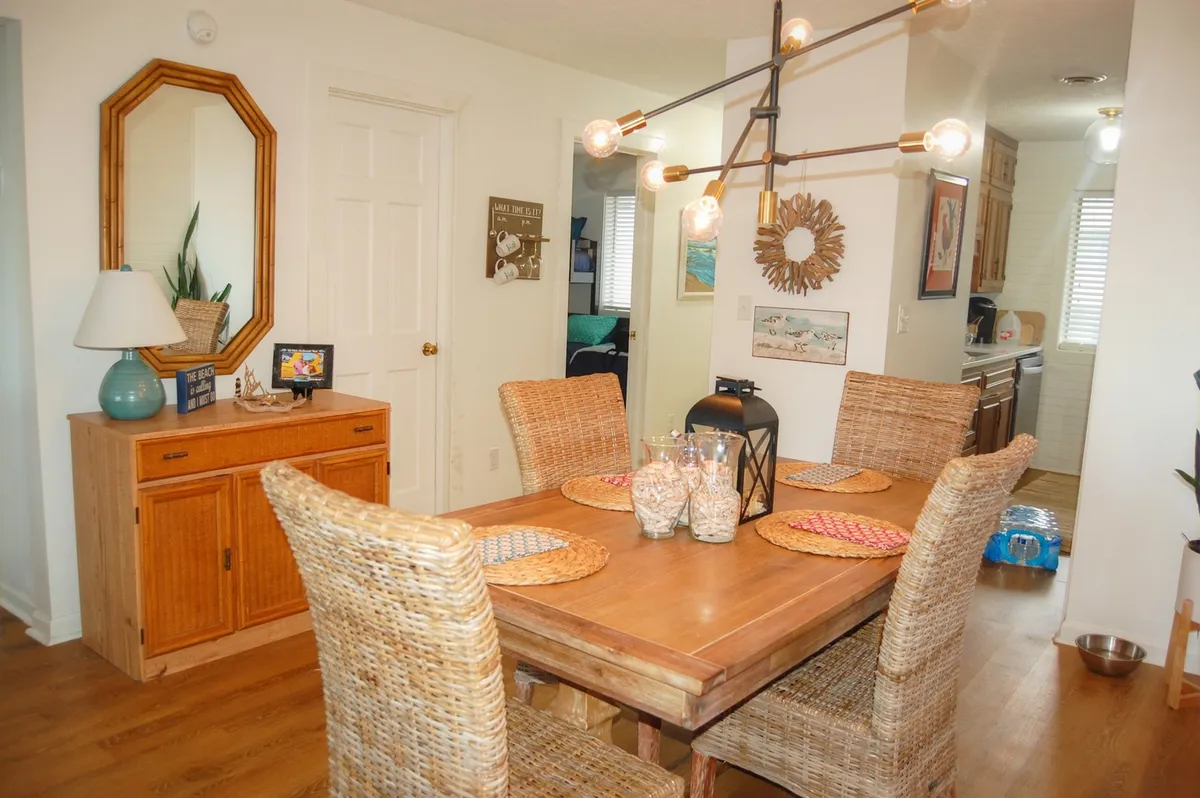 A dedicated dining area with a wooden table and woven chairs, accented by a decorative mirror, tasteful lighting fixture, and a sideboard. The atmosphere is warm and welcoming, making it ideal for shared meals and lively conversations.