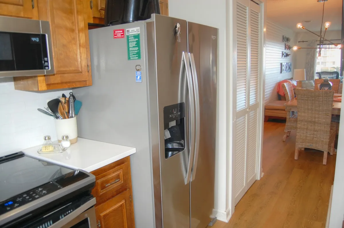 A welcoming kitchen space featuring a stainless steel refrigerator, sleek white countertops, modern wooden cabinetry, and an array of up-to-date appliances. The room is styled for both functionality and comfort, inviting guests to cook, entertain, and gather for meals. The open layout allows for easy movement and socializing.